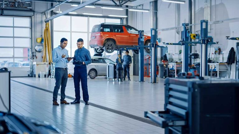 Mechanic inspecting a timing belt under the hood of a car in a bright, well-lit garage.