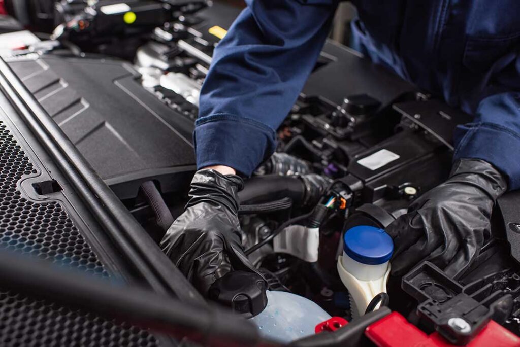Person safely connecting red and black jumper cables to two car batteries in a driveway.