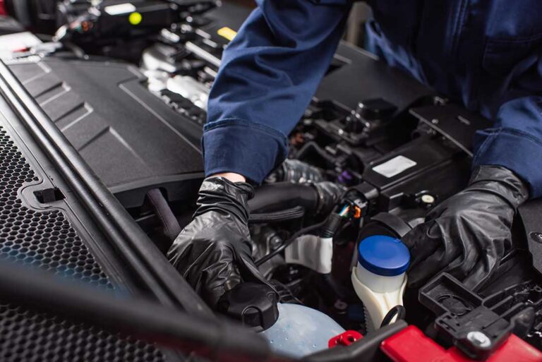 Person safely connecting red and black jumper cables to two car batteries in a driveway.