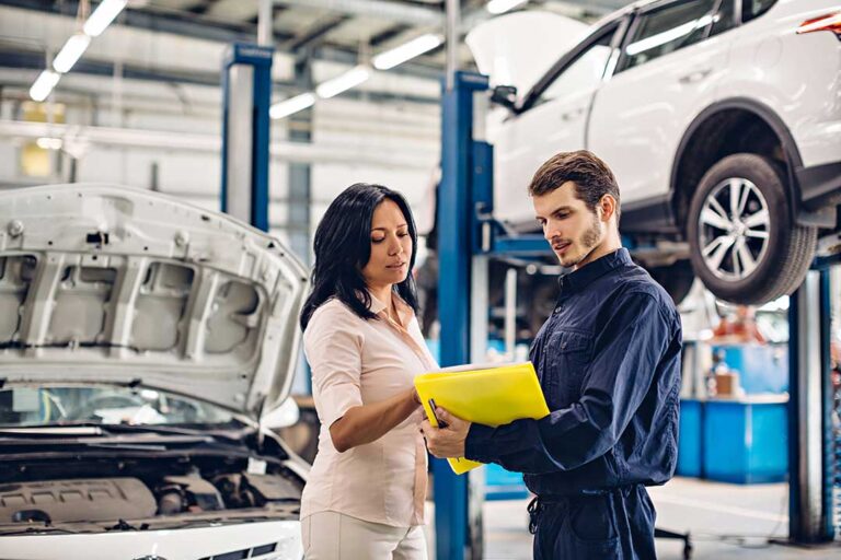 Mechanic examining a car tire and wheel while the vehicle is lifted on a shop hoist.